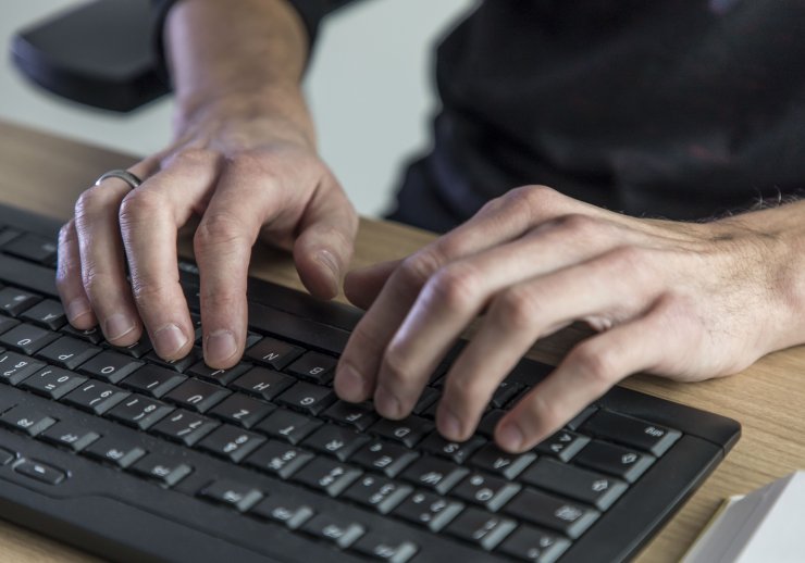 Ein Mann tippt etwas mit einer Tastatur in seinen Computer ein.