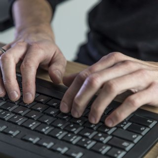 Ein Mann tippt etwas mit einer Tastatur in seinen Computer ein.