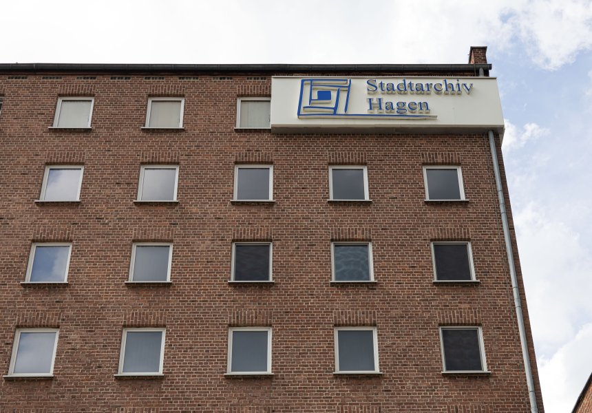 Außenansicht vom Stadtarchiv Hagen. Zu sehen ist eine Ecke eines Backsteingebäudes mit einem weißem Schild mit der blauen Aufschrift "Stadtarchiv Hagen".