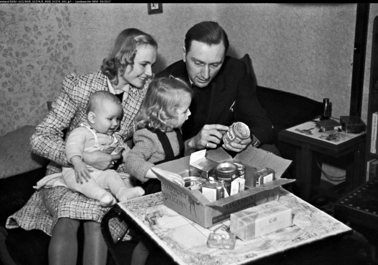 Familie, Mutter Vater und zwei Kinder, sitze an einem Wohnzimmertisch und schauen sich eine Paket mit Konserven an.
