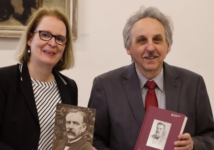 Frau Dr. Kauertz hält ein Foto von Otto Hue in die Kamera, Herr Dr. Wisotzky steht neben ihr mit dem Buch in der Hand
