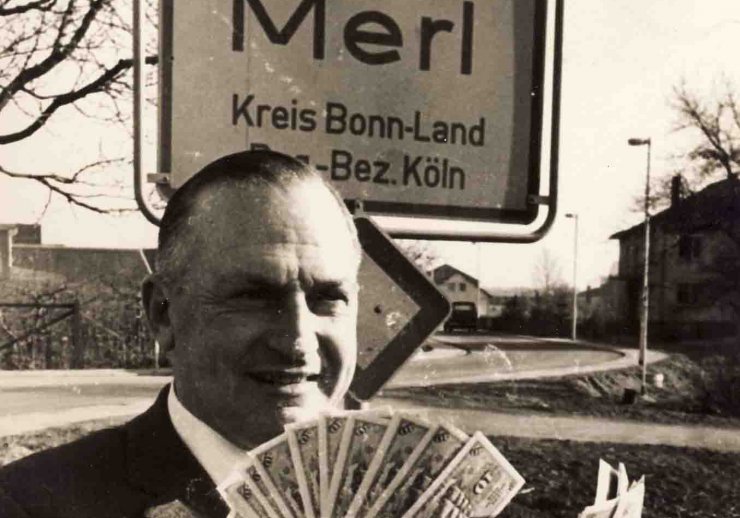 Merler Bürgermeister Gottschalk mit einem Fächer von 10-DM-Scheinen vor dem Ortsschild