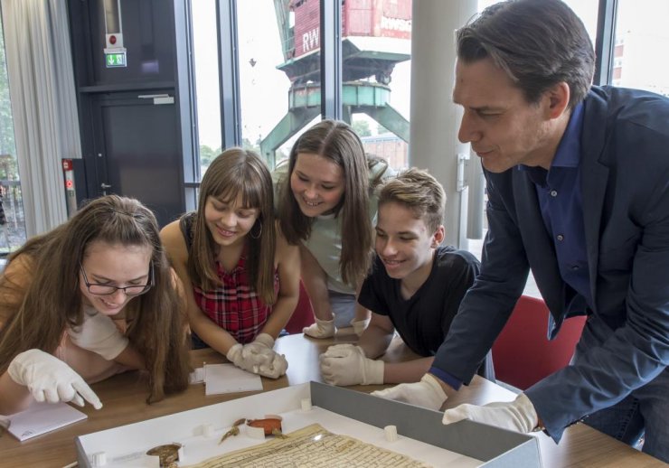 Schülerinnen und Schüler betrachten gemeinsam mit ihrem Lehrer eine Urkunde mit zwei Siegeln. 