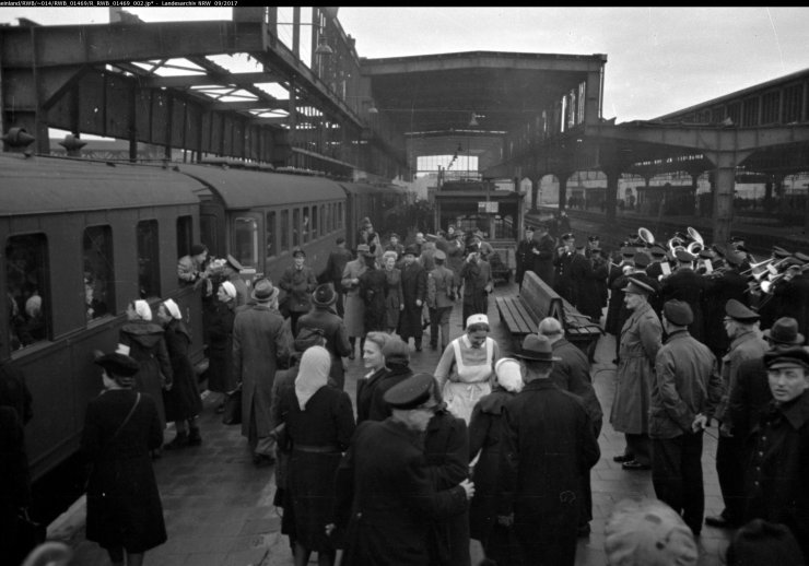 Bahnsteig mit vielen Menschen und einem abfahrenden Zug