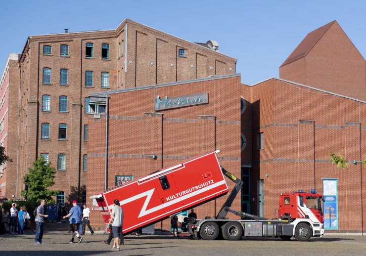 Backsteingebäude des Stadtmuseums. Auf dem Platz davor wird von einem Feuerwehrauto ein Container abgeladen auf dem Kulturgutschutz steht.