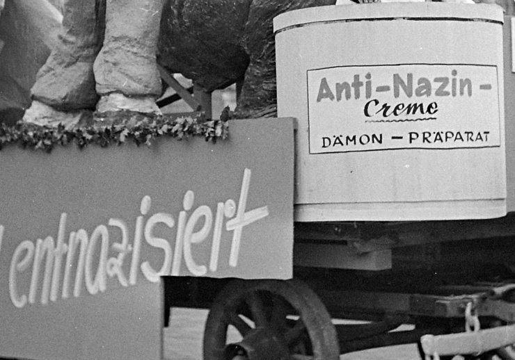 Titelbild des Flyers zur Ausstellung. Zu sehen ist ein Karnevalswagen aus den 1950er Jahren auf dem ein Patient eine Spritze bekommt. Vorne auf dem Wagen steht eine Creme betitelt mit "Anti-Nazin-Creme"