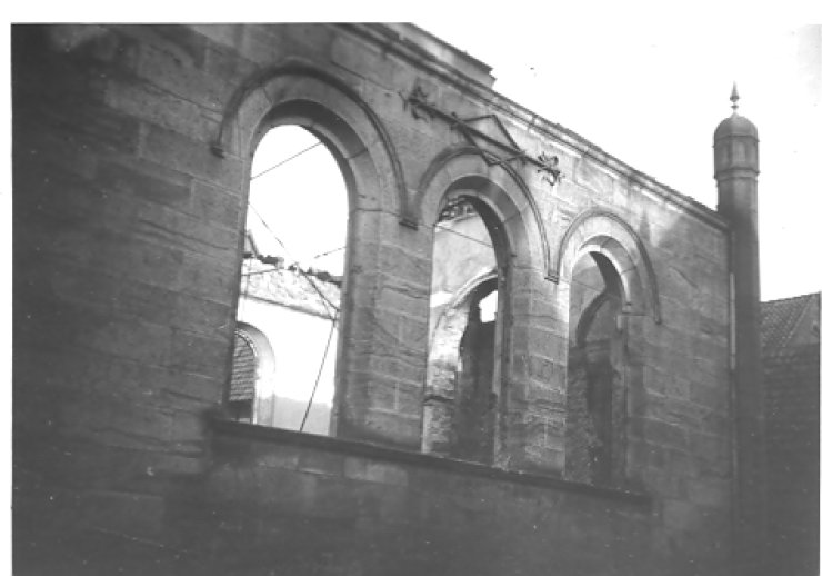 Außenwand der ausgebrannten Synagoge. Durch drei leere Fensterbögen ist der Himmel durch das offene Dach erkennbar.