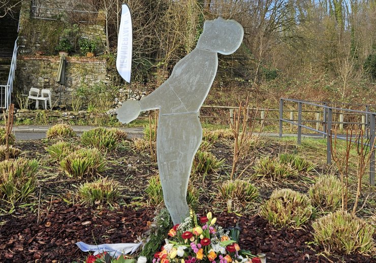 Im Vordergrund ist das Denkmal "Heller Schatten" zu sehen, an dessen Füßen Blumen niedergelegt wurden.
