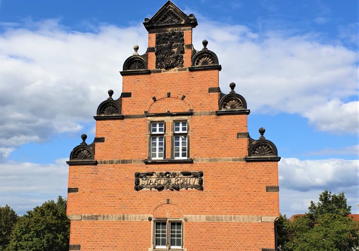 Das Bild zeigt den Giebel des alten Magazinbaus im Stil der Neorenaissance mit dem in Stein gemeisselten Schriftzug "Staatsarchivs Münster".